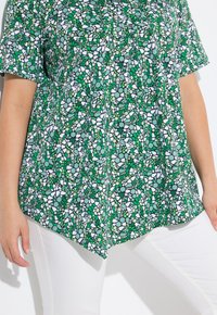 Top verde con motivo, dotato di maniche corte e orlo curvo, realizzato in tessuto leggero con accenti bianchi e verde scuro.