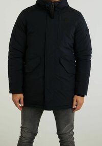 Námořnická puffer bunda se zipem, dvěma předními kapsami a kapucí. Vyrobena z měkké, strukturované tkaniny pro teplo a pohodlí.