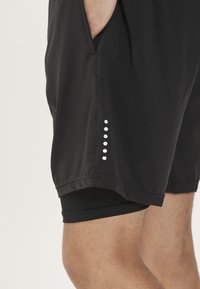 Zwarte sportshorts met een gladde textuur, voorzien van zijzakken en een hexagonaal stippenpatroon in het wit langs de zoom.