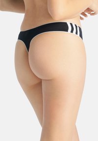 Czarny thong z białymi akcentami, charakteryzujący się gładką teksturą i minimalnym zakryciem. Bocznie prążki dodają detali eleganckiemu wzornictwu.
