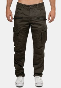 Olivgrüne Cargo-Hosen mit mehreren Reißverschlusstaschen, gesteppten Akzenten und einer schmalen Passform, aus strapazierfähigem Material. Weiße Sneaker abgebildet.
