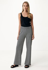 Czarny top na ramiączkach zestawiony z szerokimi spodniami w czarno-białe wzory. Spodnie mają geometryczny wzór i komfortowy krój.
