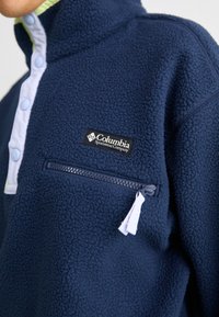 Pullover in pile blu navy con dettagli azzurri e mezza abbottonatura. Dotato di tasca sul petto con zip. Logo Columbia visibile.