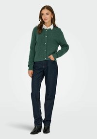 Zielony sweter z dzianiny z okrągłym dekoltem i zapięciem na guziki, zestawiony z ciemnymi dżinsami i czarnymi botkami za kostkę.