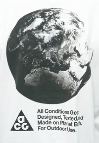 Λευκή μπλούζα με μαύρο γραφικό της Γης και κείμενο που αναγράφει «Εξοπλισμός για όλες τις συνθήκες. Σχεδιασμένο, δοκιμασμένο και κατασκευασμένο στον πλανήτη Γη.»