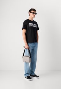 Black cotton T-shirt with white "CALVIN KLEIN" text, light blue denim jeans, gray bag with dark strap, and black shoes with white sole.