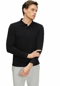 Schwarzes Langarm-Polohemd mit Kragen, ausgestattet mit einer Drei-Knopf-Blende, getragen mit hellgrauen Jogginghosen. Glatte Stoffoberfläche.