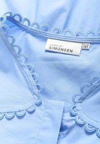Blusa azzurro chiaro con scollatura ondulata e delicata ricamo. L'etichetta recita "KAREN BY SIMONSEN," EU 38 US 8. Tessuto morbido e liscio.