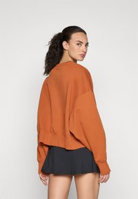 Túlméretezett rozsdabarna pulóver, amely pamut keverék szövetből készült, ejtett vállakkal, bordás mandzsettákkal és cropped hem-mel, fekete szoknyával párosítva.