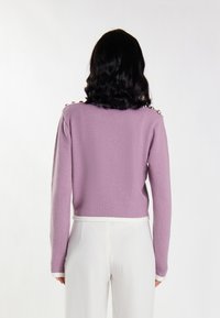 Lila cropped trui met lange mouwen, textuur breiwerk en witte rand langs de onderkant en manchetten. Decoratieve knopen op de schoudernaad.