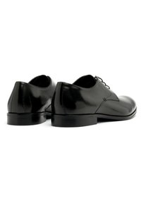 Chaussures habillées en cuir noir avec une finition brillante, un bout rond et un talon bas, présentant des détails de couture subtils sur les côtés.