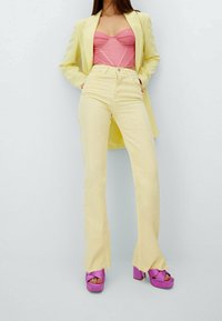 Gele uitlopende broek, roze korsettop en paarse plateauzolen met hoge hakken. De outfit wordt compleet gemaakt met een op maat gemaakte gele blazer.