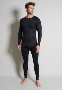 Ensemble de couche de base thermique noire comprenant un haut à manches longues et un legging, fabriqué en matériau lisse et extensible avec des poignets côtelés.