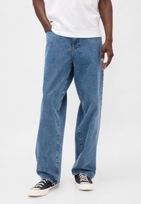 Ohlapne modre denim hlače z izpiranjem, s petimi žepi in ravnim krojem nogavic, dopolnjene s črnimi platnenimi supergami.