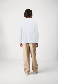 White long-sleeve shirt and beige wide-leg pants with a smooth texture. Shirt has a simple crew neckline and relaxed fit.