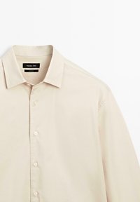 Beżowa koszula z guzikami, o klasycznym kołnierzyku, wykonana z gładkiej bawełny, z delikatnym połyskiem. Posiada guziki z przodu i metkę z napisem "Massimo Dutti".