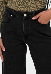Černé džíny z denimu s vysokým pasem, pěti kapsami a mírně zúženou nohavicí. Obsahují kovový knoflík a kontrastní prošití.