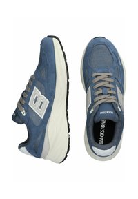 Mėlyni zomšiniai ir tinkliniai sportbačiai su balta guma, pilkomis raištelėmis ir išskirtiniu logotipu šone. Apvalus priekis ir paminkštinta konstrukcija.