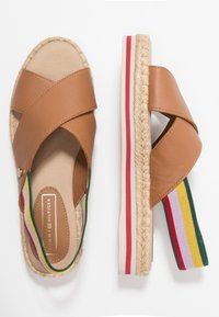 Espadrille en cuir brun avec des brides croisées, semelle en jute tressé et accent élastique rayé multicolore au niveau du talon.