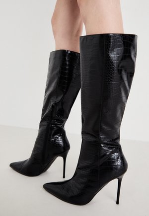 Bottes noires en cuir verni, montantes jusqu'au genou, avec une texture crocodile, un bout pointu, un haut talon aiguille et un détail de fermeture éclair sur le côté.