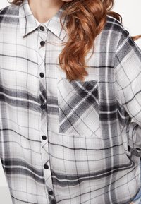 Camicia a bottone a quadri in bianco e nero realizzata in tessuto leggero, con una tasca a toppa e motivi a quadri contrastanti.