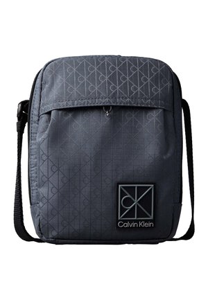 Sac bandoulière Calvin Klein gris foncé avec un motif monogramme subtil, poche avant zippée et sangle noire ajustable.