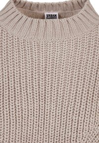 Pull en tricot beige avec un motif texturé, doté d'un col rond côtelé et d'un fil épais. Étiquette visible : « URBAN CLASSICS. »