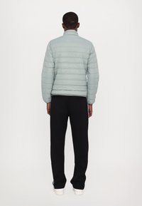 Light blue puffer jacket with quilted texture, high collar, and elastic cuffs, paired with black pants and white sneakers.