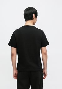 Čierne tričko s krátkym rukávom a okrúhlym výstrihom, vyrobené z hladkej bavlny, s voľným strihom a minimalistickým dizajnom.