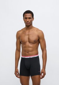 Μαύρα ανδρικά εσώρουχα boxer με γκρι και ροζ μέση που φέρει το λογότυπο «NIKE». Κατασκευασμένα από απαλό ύφασμα, διαθέτουν ελαστική εφαρμογή και μήκος μέχρι το μέσο του μηρού.