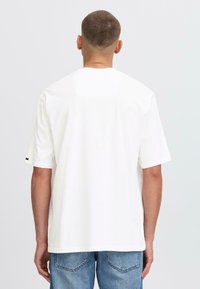 White short-sleeve t-shirt, crew neckline, smooth cotton fabric, back view showing plain design, worn with light blue denim jeans.