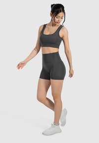 Sujeción deportiva gris oscuro y pantalones cortos de cintura alta hechos de material elástico. Diseño ajustado, textura suave, con tirantes y un acento de logo.