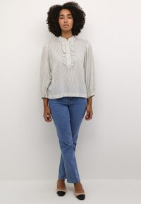 Blouse légère à rayures avec un plastron froncé et des manches longues, associée à un jean bleu et des escarpins beiges avec un embout noir.