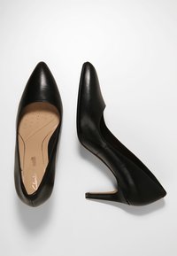 Chaussures noires en cuir à talons hauts avec un bout pointu et une texture lisse. L'intérieur présente un design perforé pour une meilleure respirabilité.