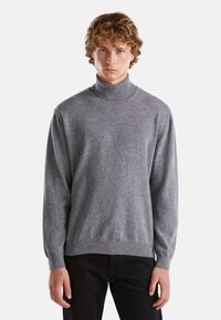 Maglione grigio a collo alto realizzato in morbido tessuto a maglia, con maniche lunghe e vestibilità rilassata, abbinato a pantaloni neri.