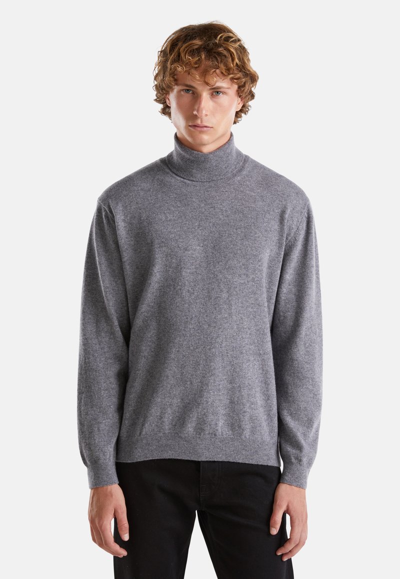 Maglione grigio a collo alto realizzato in morbido tessuto a maglia, con maniche lunghe e vestibilità rilassata, abbinato a pantaloni neri.