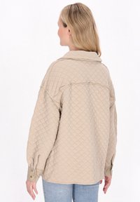 Beige gesteppte Jacke mit Kragen, strukturiertem Muster, langen Ärmeln und geknöpften Manschetten. In einem lässigen Schnitt, der bis zur Hüfte reicht.