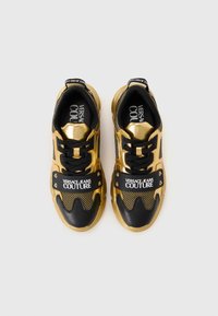 Sorte og guld sneakers med en mesh overdækning, læderdetaljer og en fremtrædende rem med "VERSACE JEANS COUTURE" logo.