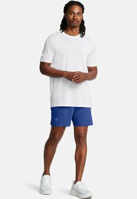 Camisa deportiva de manga corta blanca, pantalones cortos azules, zapatillas blancas. La camisa tiene un escote redondo; los pantalones cortos tienen un logo de Under Armour.