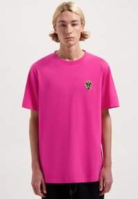 Felle roze T-shirt met korte mouwen, voorzien van een klein, multicolor geborduurd ontwerp op de linkerborst. Zachte, gladde stof met een comfortabele pasvorm.