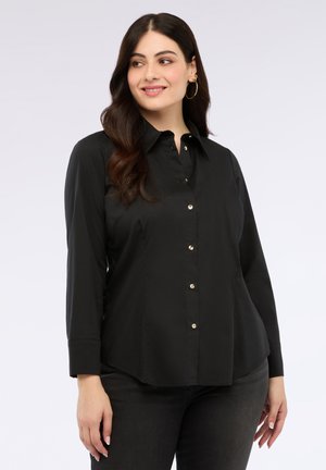 Chemise noire à manches longues, col classique et ourlet arrondi. Présente des boutons dorés et une texture de tissu lisse.