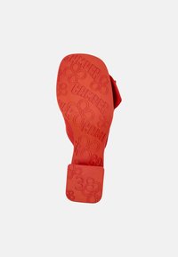 Red rubber sandal sole featuring a textured pattern with "Camper" branding, flower motifs, and a square heel marked with size 38.