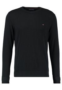 Schwarzer Pullover mit langen Ärmeln aus weichem Material, mit einem runden Halsausschnitt und gerippten Bündchen, versehen mit einem kleinen rot-weißen und blauen Logo auf der Brust.