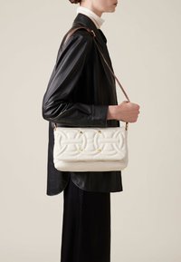 Sac en bandoulière blanc matelassé avec des accents dorés, de forme rectangulaire, porté sur une veste en cuir noir.