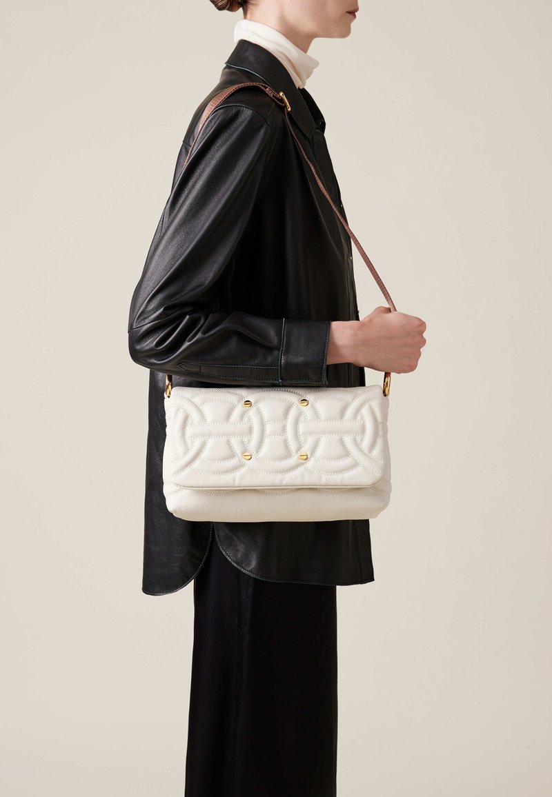 Sac en bandoulière blanc matelassé avec des accents dorés, de forme rectangulaire, porté sur une veste en cuir noir.