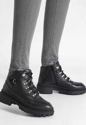Czarne skórzane botki do kostki z teksturowaną powierzchnią, sznurowaniem, srebrnymi przelotkami i masywną gumową podeszwą zapewniającą przyczepność.