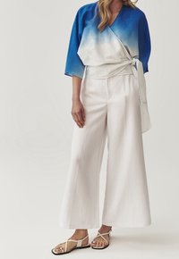 Top envolvente en degradado azul y blanco con mangas de tres cuartos, combinado con pantalones anchos blancos y sandalias planas beige.