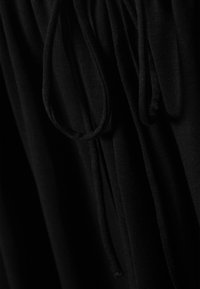 Tissu noir à la texture douce, doté de cordons, de sections froncées et de plis, mettant en avant un design décontracté et fluide.