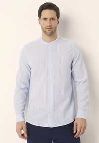 Camicia a maniche lunghe di colore azzurro chiaro con righe bianche verticali, colletto alla cinese e bottoni frontali. Tessuto morbido con una vestibilità casual.