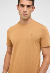 Beżowy t-shirt z okrągłym dekoltem, wykonany z miękkiej bawełny, z krótkimi rękawami; posiada delikatne haftowane logo na lewej piersi.